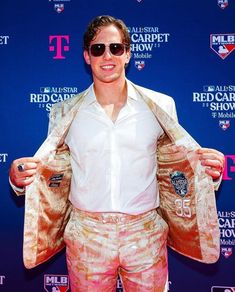 a man in white shirt and pink shorts holding up his jacket on the red carpet