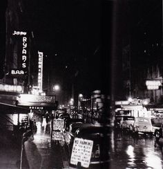 a black and white photo of cars on a city street at night with neon signs