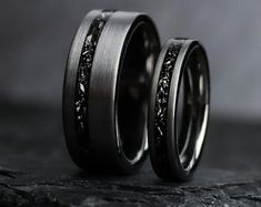 two wedding bands with black diamonds in them on top of a stone slabd surface