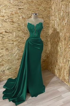 a green evening gown on display in front of a wooden wall with straw balks