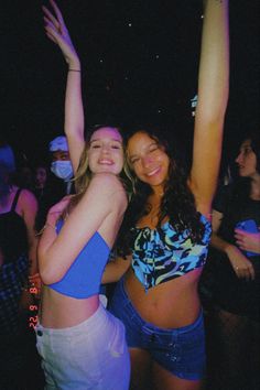 two women standing next to each other in front of a crowd at a nightclub with their arms up