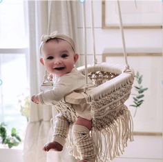 a baby is sitting on a swing in the living room and smiling at the camera