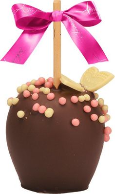 a chocolate covered apple with pink and white sprinkles on the top, topped by a wooden stick