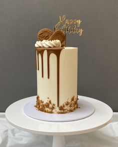 a birthday cake decorated with frosting and chocolate on a white pedestal in front of a gray background