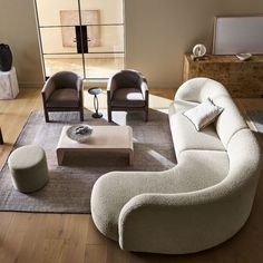 a living room filled with furniture on top of a hard wood floor covered in white rugs