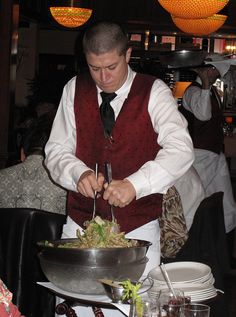 a man in a vest and tie is cutting into a salad at a table with other people