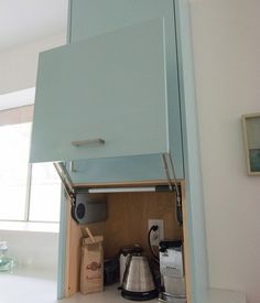 an open cabinet in the corner of a kitchen with coffee pots and tea kettles