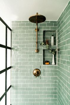 a green tiled shower with gold fixtures and shelves on the wall, along with vases