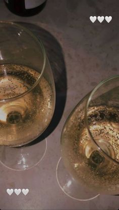 two wine glasses filled with liquid sitting on top of a table next to each other