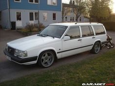 a white station wagon parked in front of a blue house with a motorcycle next to it