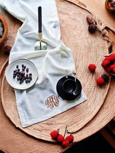 a table topped with plates and bowls filled with berries next to a white napkin on top of a wooden table