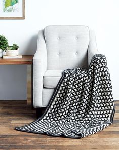 a white chair with a black and white blanket on it next to a wooden table