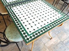 a table with green and white tiles on it, surrounded by metal chairs in a restaurant