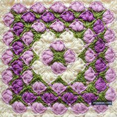 a crocheted square with purple and white flowers in the center on top of it