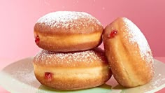 three donuts on a plate with powdered sugar sprinkled over them and strawberry jam in the middle