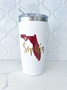 a white travel mug with the word souvenia printed on it and a straw in its mouth