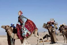 a group of people riding on the backs of camels in the desert with no one around them