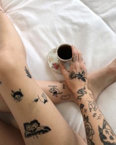 a woman with tattoos on her legs holding a coffee cup and saucer while laying in bed