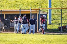 a group of baseball players standing on top of a field next to home plate in front of a fence