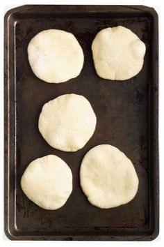 four uncooked pizza doughs on a baking sheet