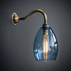 a wall light with a blue glass shade on it's arm and an antique brass finish