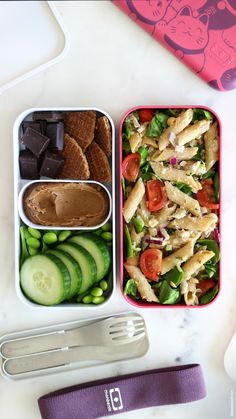 a lunch box filled with pasta, cucumber slices and other foods next to a fork