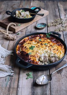 a casserole dish with meat and vegetables in it on a wooden table next to two serving spoons