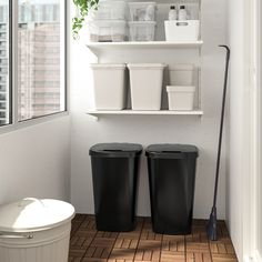 two black trash cans sitting next to each other on a tiled floor in front of a window