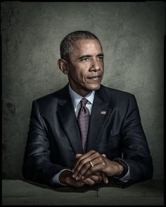 a man in a suit and tie sitting at a table with his hands folded out