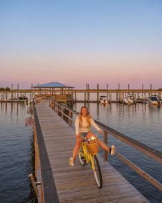 a woman sitting on a yellow bike next to a pier with boats in the water