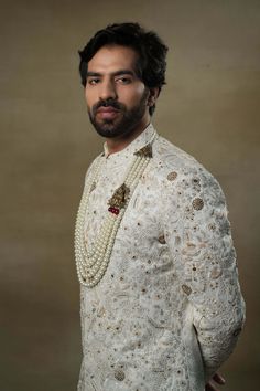 Editor's Note Featuring our work of art in our white all over hand-embroidered sherwani set. The foundation is crafted using machine embroidery adorned with tone on tone thread serving as the base texture, while the second tier showcases highlighting with 3D brass elements, dabka and zari threads. Fabric: Linen silk Color: Ivory, gold Components: Sherwani, kurta and churidar Occasion: Groom Fit: Regular Note: Product colour may slightly vary due to photographic lighting sources Care: Dry clean o Festive Sherwani With Gold Embroidery For Transitional Season, Festive Gold Embroidered Sherwani For Transitional Seasons, Transitional Festive Sherwani With Gold Embroidery, Ceremonial Sherwani With Intricate Embroidery In Raw Silk, Festive Sherwani With Gold Embroidery And Traditional Drape, Elegant Resham Embroidery Nehru Jacket For Traditional Ceremonies, Off White Raw Silk Set With Intricate Embroidery, Elegant Nehru Jacket With Resham Embroidery For Ceremonies, Raw Silk Bandhgala With Intricate Embroidery For Traditional Ceremonies