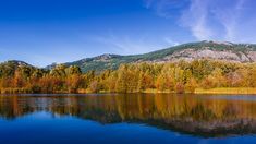 a lake surrounded by trees with mountains in the background and autumn foliage on the bank