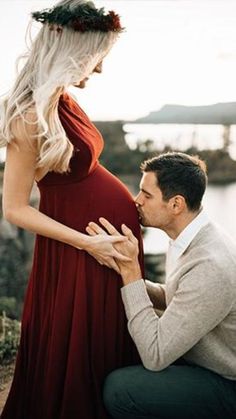 a man kneeling down next to a woman in a red dress and holding her belly