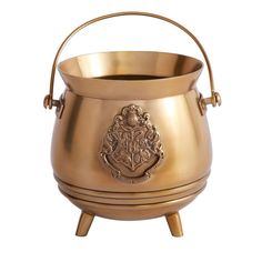 a golden metal pot with a crest on the front and legs, sitting on a white background