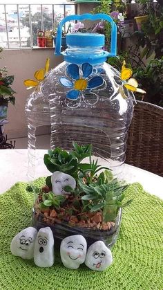 a plastic water bottle sitting on top of a table next to plants and rocks with faces drawn on them