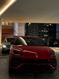 two cars are parked in front of a building at night, one is red and the other is black