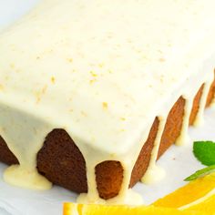 a close up of a cake with icing and orange slices on a plate next to a slice of lemon