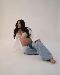 a pregnant woman sitting on the ground in jeans and a white shirt with her legs crossed