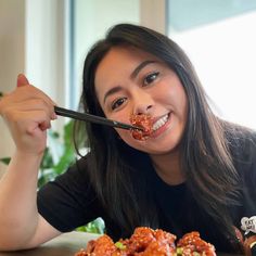 a woman is eating spaghetti with chopsticks in her mouth and smiling at the camera