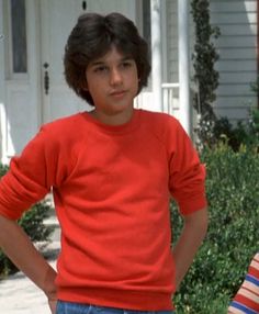 a young boy standing in front of a house with his hands on his hips and looking at the camera