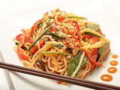 a white plate topped with noodles and veggies next to chopsticks on a table