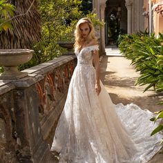 a woman in a white wedding dress standing on a stone wall with palm trees behind her