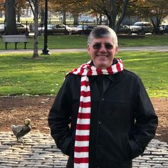 an older man wearing a red and white scarf standing in front of a park bench