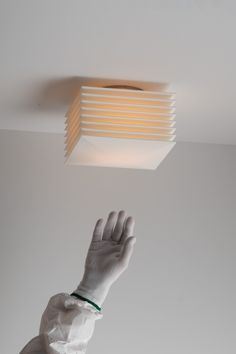 a gloved hand reaching up to a light fixture in a room with white walls