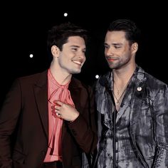 two men standing next to each other in front of a black background with white lights