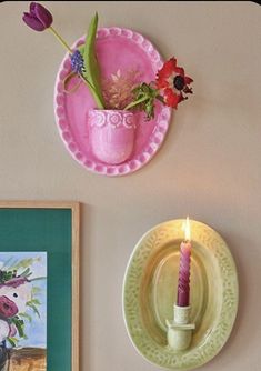 two plates with flowers and a candle on them are sitting next to a wall hanging