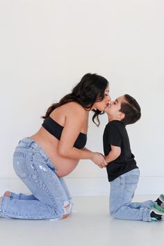 a woman kneeling down next to a little boy on the ground kissing her face with both hands