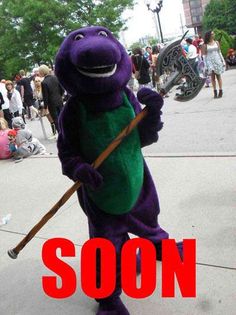 a person in a purple dinosaur costume holding a stick with the words soon on it