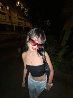 a woman with sunglasses on walking down the street in shorts and tank top at night