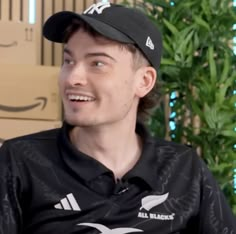 a young man wearing a black hat sitting in front of a cardboard box and looking off to the side